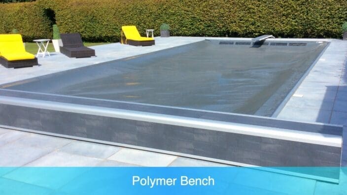 Covered rectangular swimming pool sits under a taut dark safety cover, surrounded by a tiled patio with yellow-cushioned lounge chairs and trimmed hedges in the background. Transcribed text: Polymer Bench