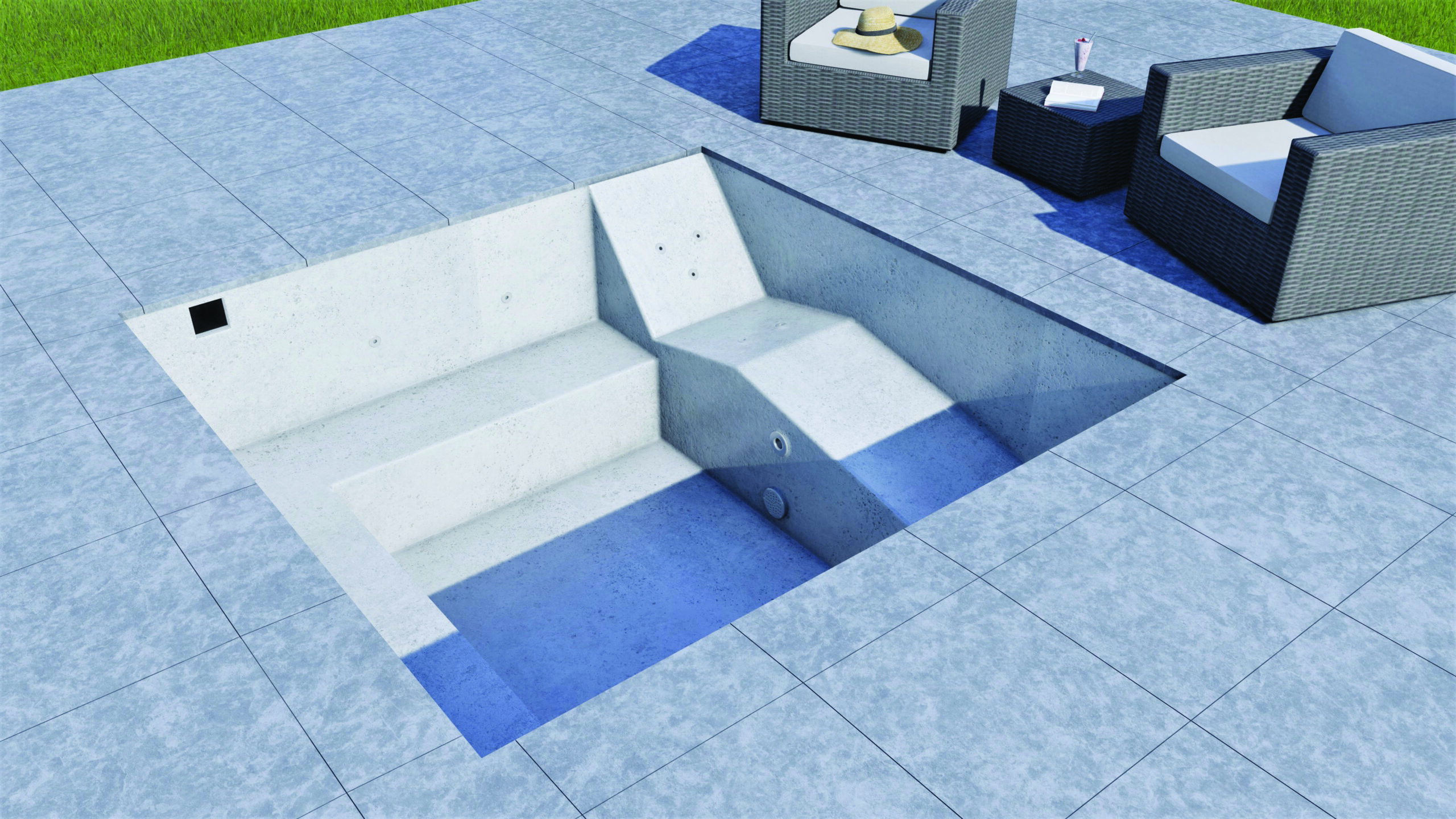 A sunlit recessed concrete plunge pool sits partly filled with blue water, showing built-in steps and bench; it's set within light-gray tiled patio beside wicker lounge chairs and green lawn.