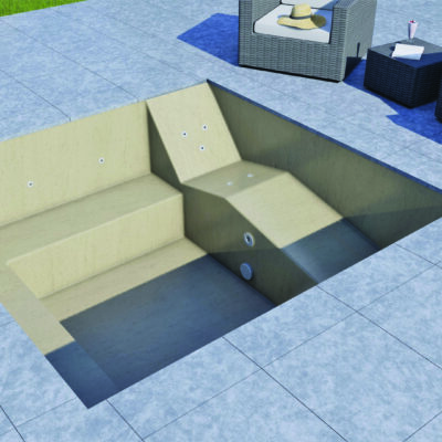 An empty sunlit plunge pool sits recessed into a tiled patio, showing steps and jets, with nearby wicker lounge chairs, side table with a hat, drink and lawn.