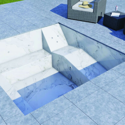 A recessed marble pool sits empty, revealing built-in steps, bench seating and jets, set in a tiled patio beside wicker armchairs, a side table with hat and drink and lawn.