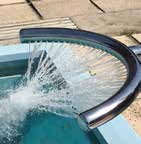 Curved stainless-steel pool handrail channels a spray of water into the pool, creating a splash and concentric ripples beside tiled coping on a sunlit concrete deck.