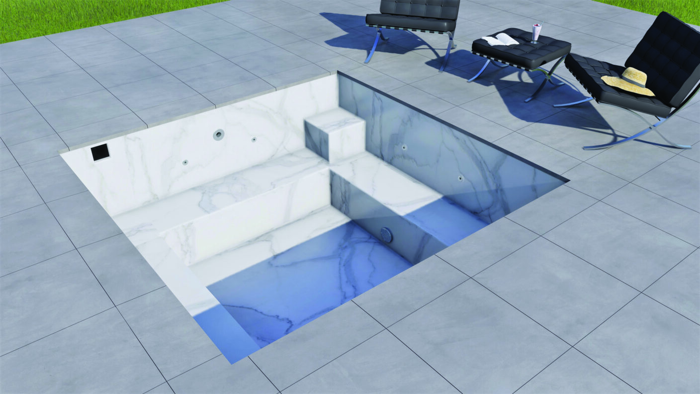 Rectangular marble plunge pool sits recessed in a tiled patio, holding shallow blue water over steps; nearby black leather lounge chairs, hat and drink on the deck, grassy edge beyond.
