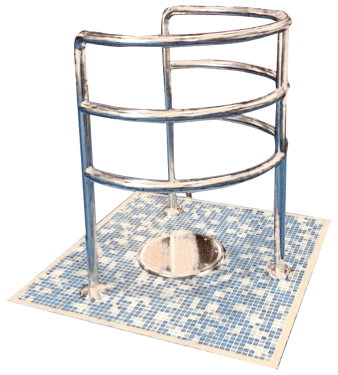 A chrome three tier handrail encircles a recessed stainless squat pan mounted on a square of small blue and white mosaic tiles, suggesting an accessible bathroom fixture.