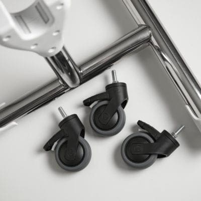 Three black-and-gray office chair caster wheels lie beside a chrome chair base and white seat component on a white surface; one caster shows a small locking tab.