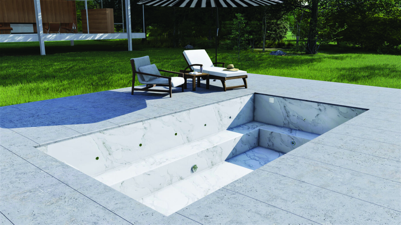 Empty marble-lined plunge pool sits recessed in tiled patio; two lounge chairs and small table with hat under striped umbrella beside it; grassy lawn and house beyond.