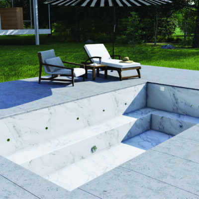 Empty marble-lined plunge pool sits recessed in tiled patio; two lounge chairs and small table with hat under striped umbrella beside it; grassy lawn and house beyond.