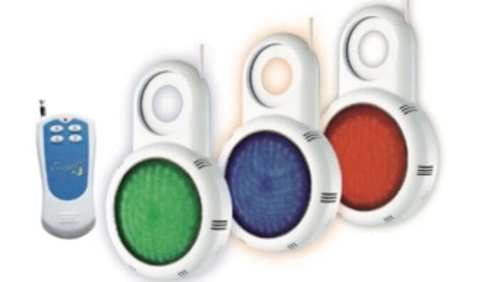 Three round LED fixtures glow green, blue, and red while suspended by white plastic hooks, accompanied by a small white remote control positioned to their left on a white background.