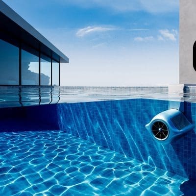 Oval wall-mounted pool control displays 60°F while a blue underwater skimmer circulates water along the tiled pool wall beside a modern glass-walled house under a clear sky.