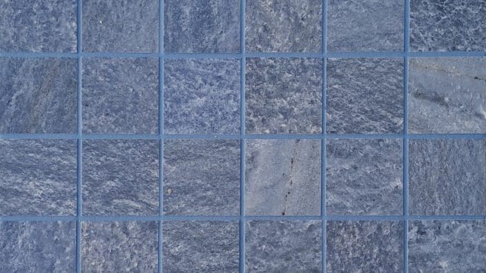 Blue square stone tiles form a neat grid, each textured tile separated by thin grout lines, creating a uniform tiled surface resembling a wall or floor